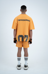 Model in the Haresquare Apricot Tan T-shirt with a grey print, styled with Haresquare Apricot Tan shorts and designer sunglasses – unisex luxury sportswear from Ireland.